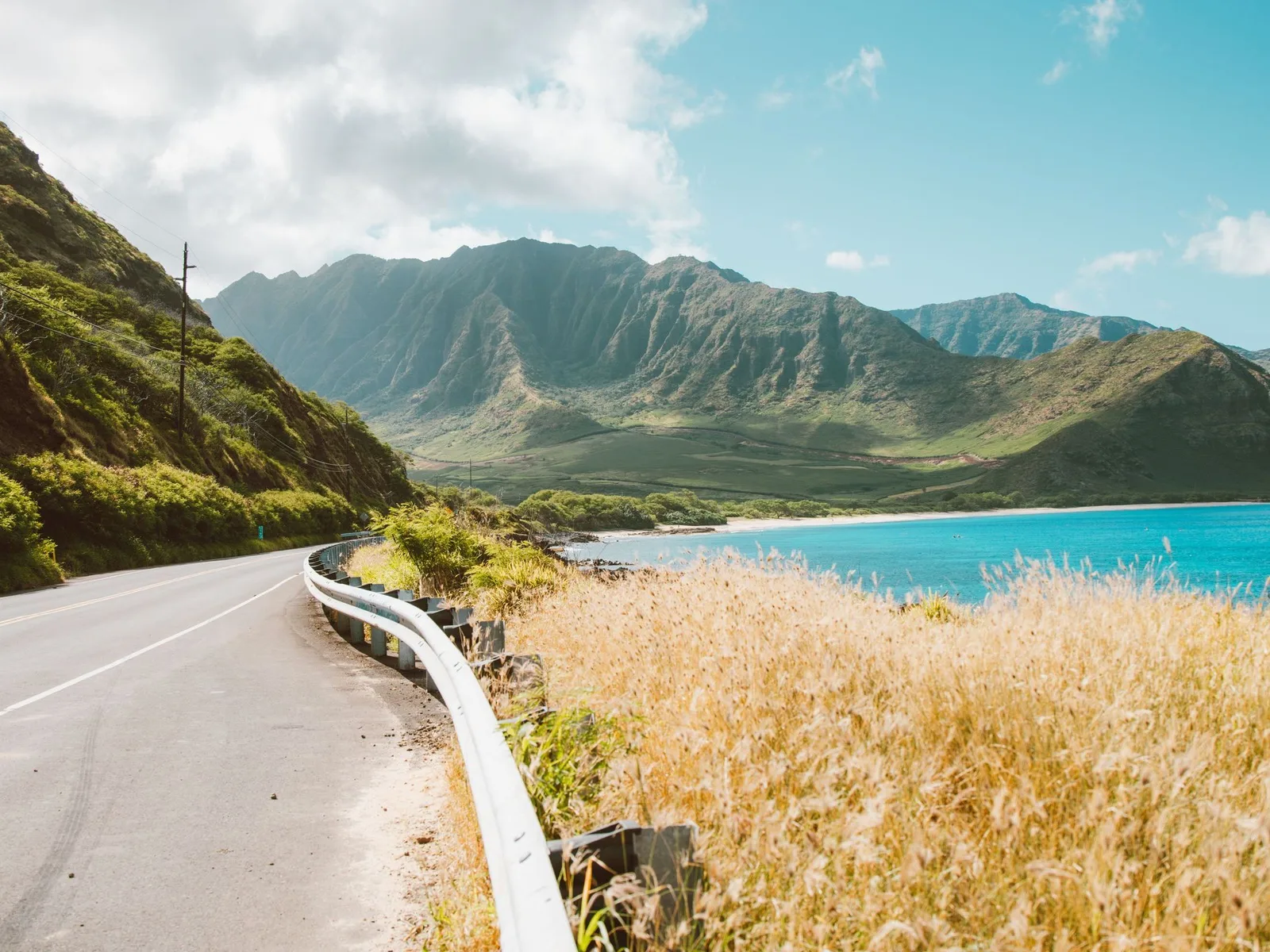 A coast road running along a steep green shoreline above a turquoise bay