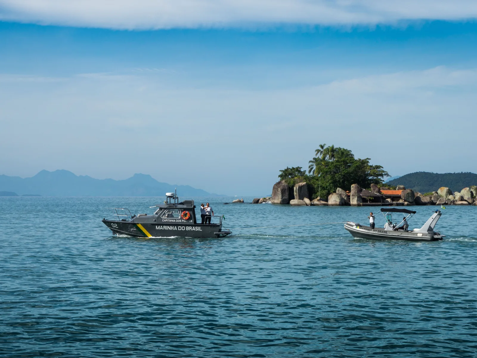 Boats on the flat green water of Paraty Bay with a small forested island behind them and the mainland ridges beyond