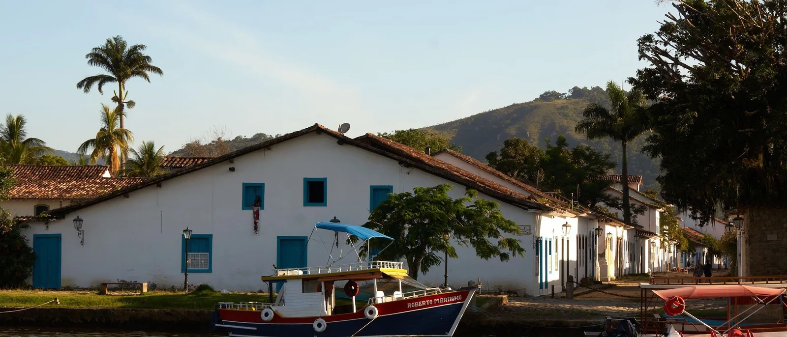 Paraty’s waterfront seen across the water, a wooden boat moored in front of whitewashed colonial houses with blue window frames