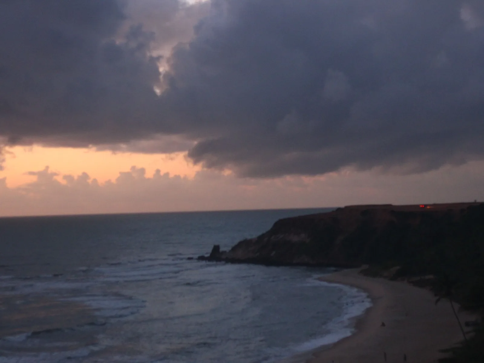 Dawn breaking over the headland at Praia do Amor, heavy cloud above a dark sea and the wet sand of the empty beach catching the first light