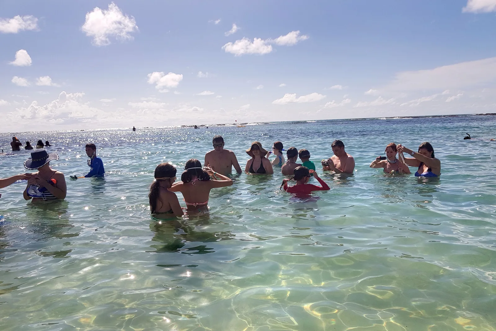 A group of people standing and sitting in a shallow natural pool at Porto de Galinhas, the water clear enough to see the reef bed under them