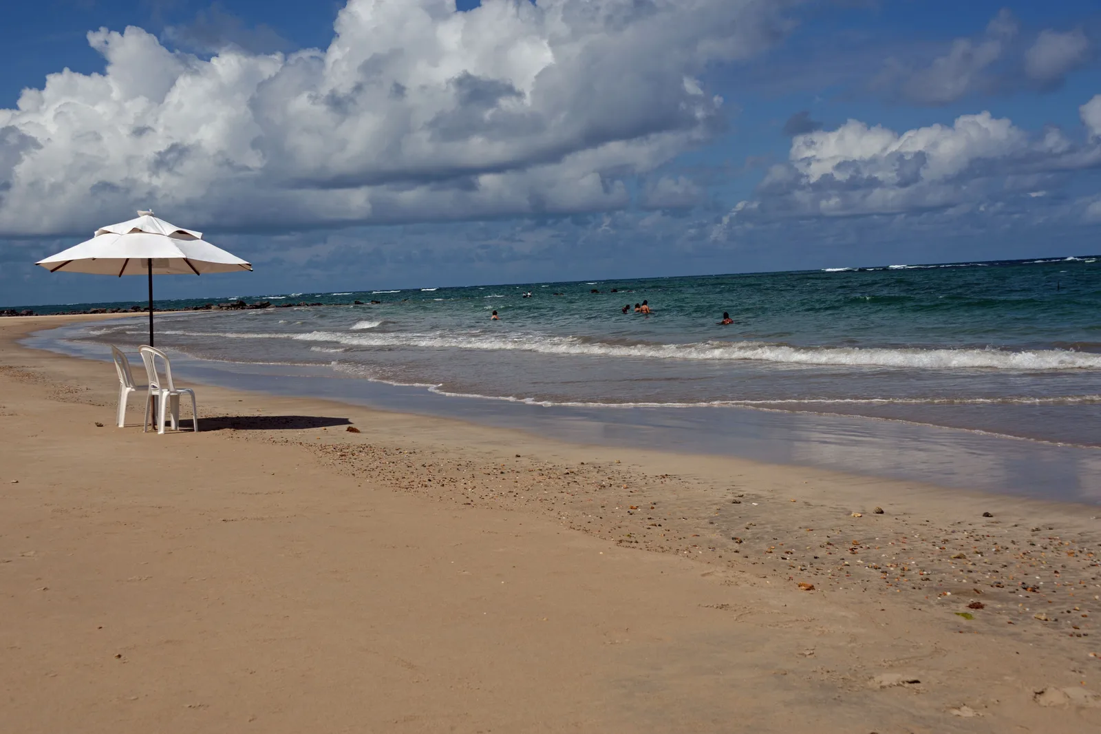 An empty beach at Serrambi with a single white umbrella and two plastic chairs set out on the sand under a heavy sky