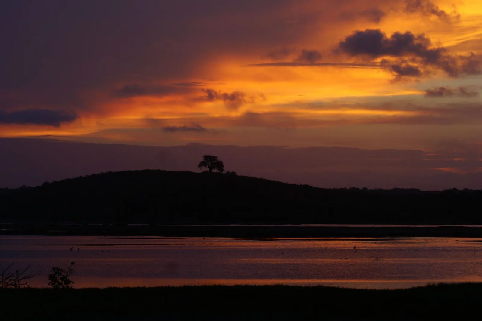 A burning orange dusk sky over a dark headland and still water at Porto de Galinhas