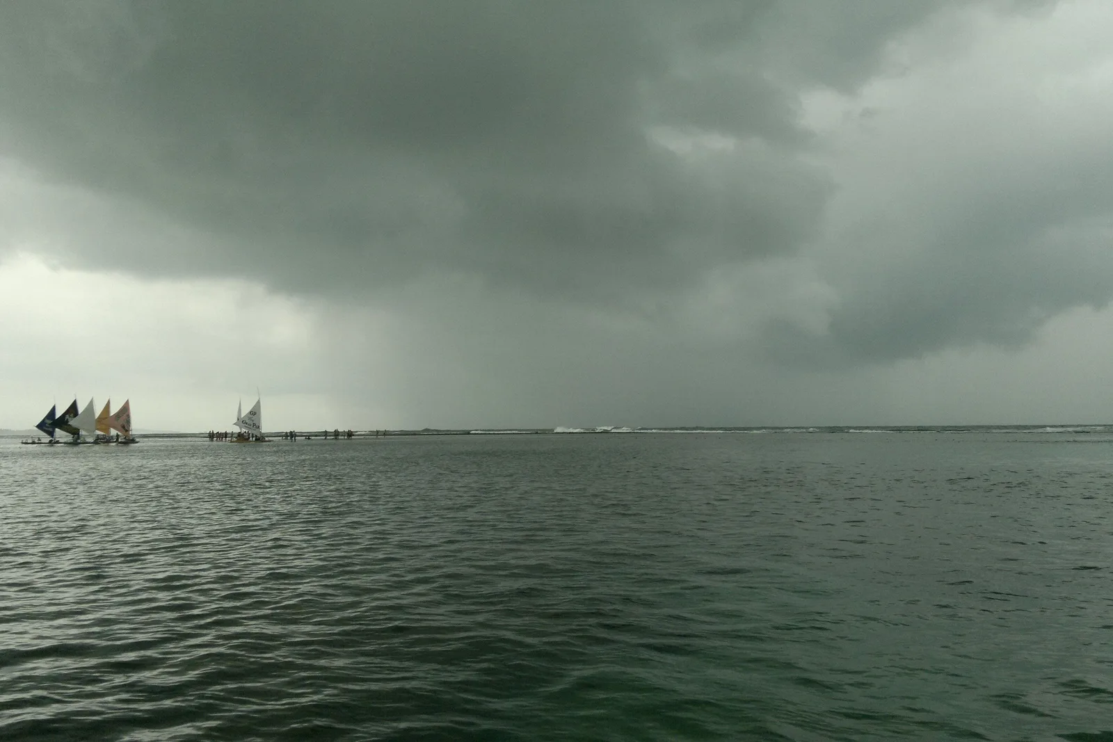 Flat gray water at Porto de Galinhas on an overcast day, a handful of jangadas small on the horizon