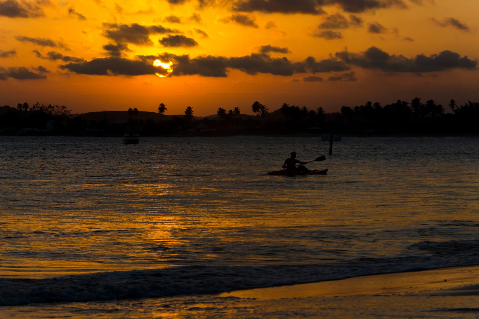 Sunset over the water at Serrambi, a lone paddler silhouetted against the light on the flat sea