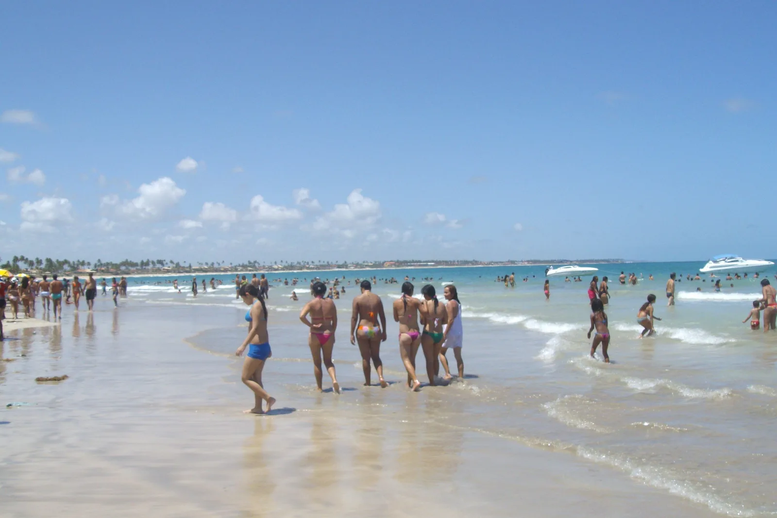 Vacationers standing and walking in the clear shallow water at Porto de Galinhas in large numbers on a bright day