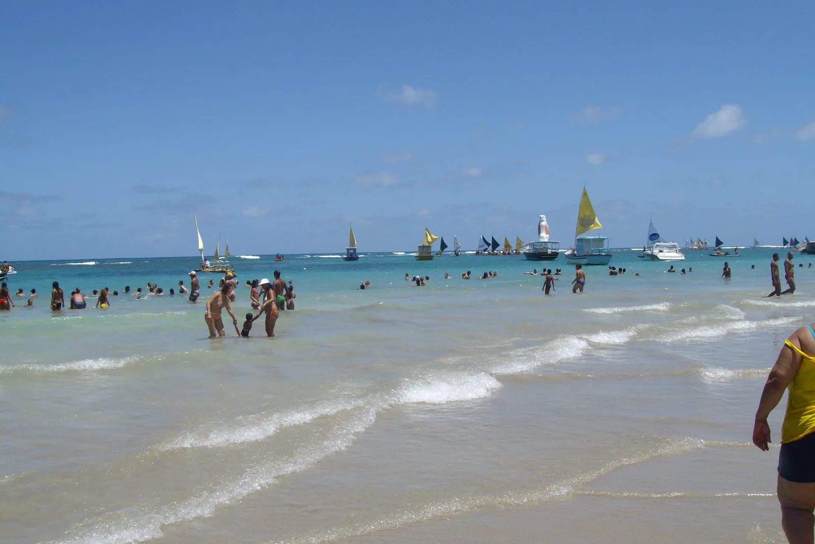 People standing waist-deep in the shallows at Porto de Galinhas with jangadas anchored in a line further out