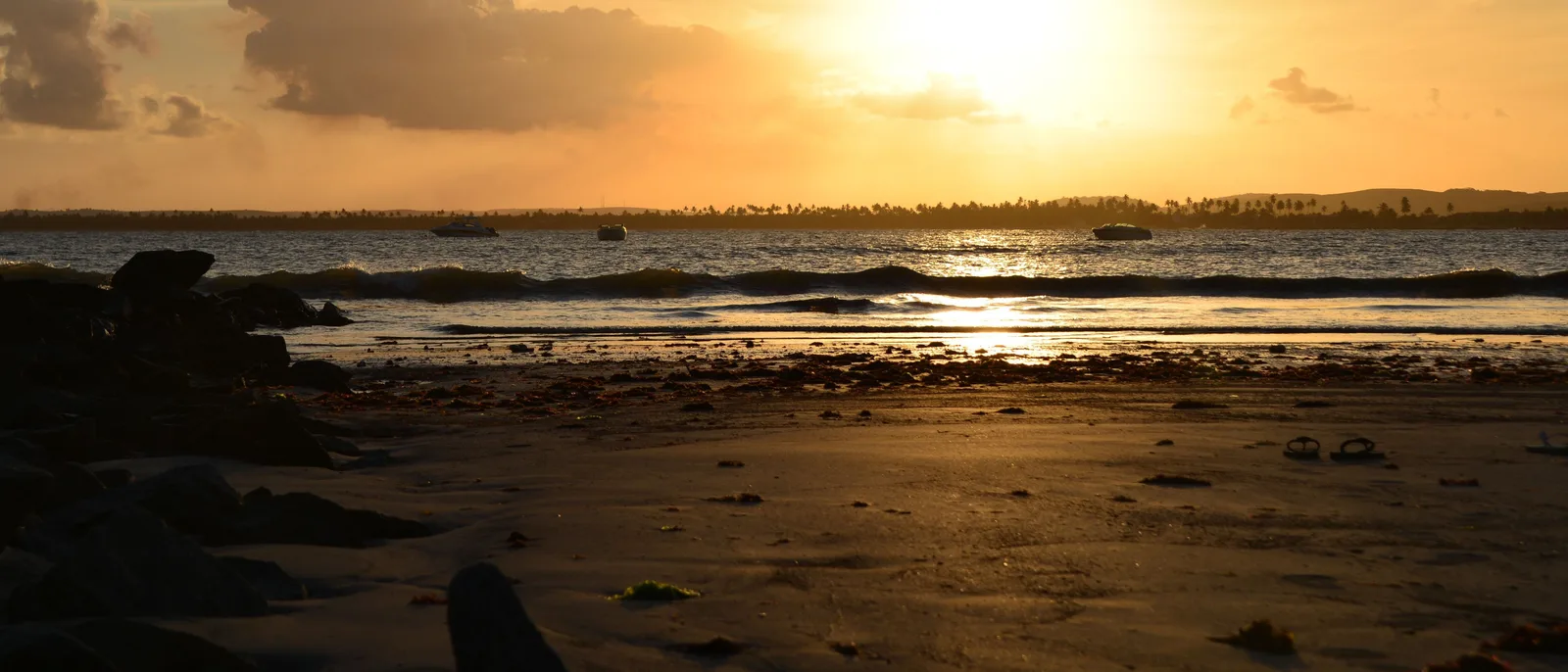Sunset over the wet reef flats at Serrambi, the sun low behind cloud and the exposed rock dark against pale water