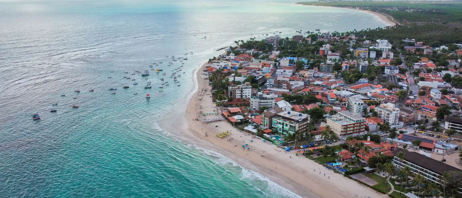 The beach at Porto de Galinhas from the air, jangadas moored in a line on turquoise water and the red roofs of the village packed along the sand behind