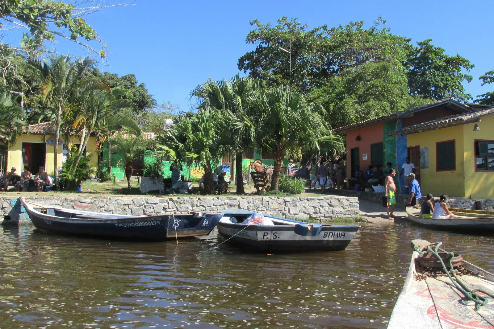 Wooden canoes moored along the Rio Caraíva in front of the village, low yellow and green painted houses and palms on the bank behind