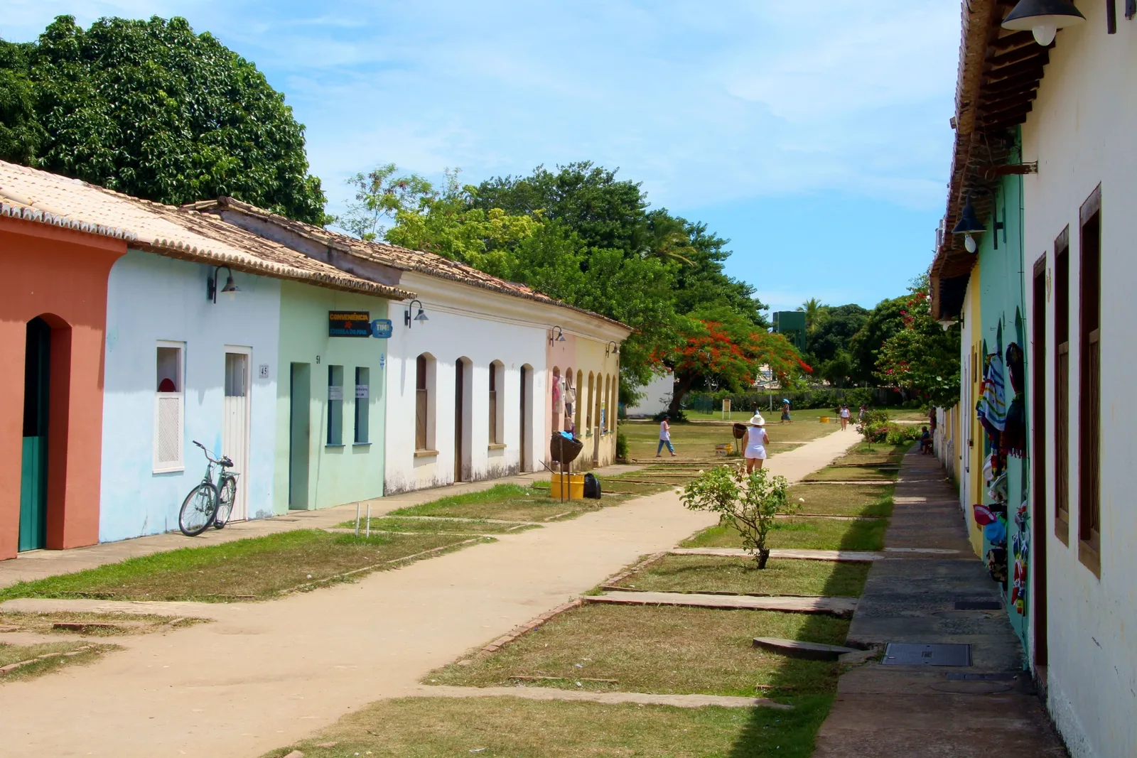 A street in Porto Seguro’s Cidade Alta: low colonial houses painted white, green and pink along a wide sandy path with a strip of lawn, a bicycle leaning by one door