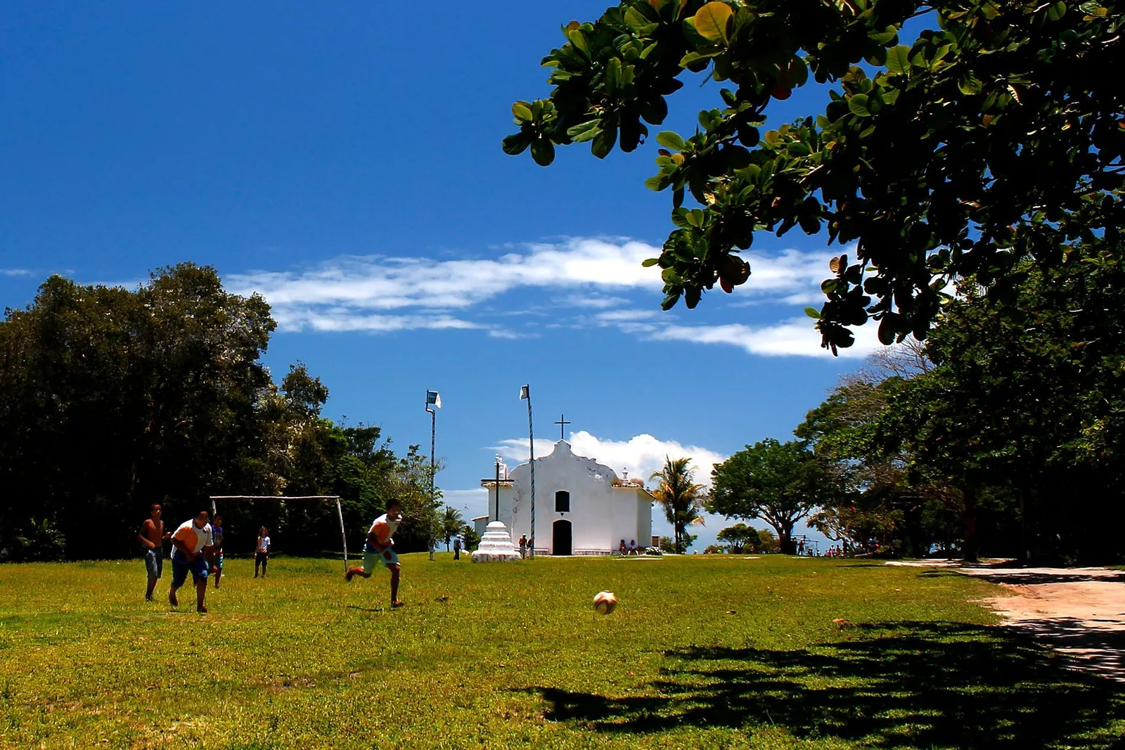 The wide green of Trancoso’s Quadrado with the white church far off at the end, a football goal and people playing on the grass under a deep blue sky