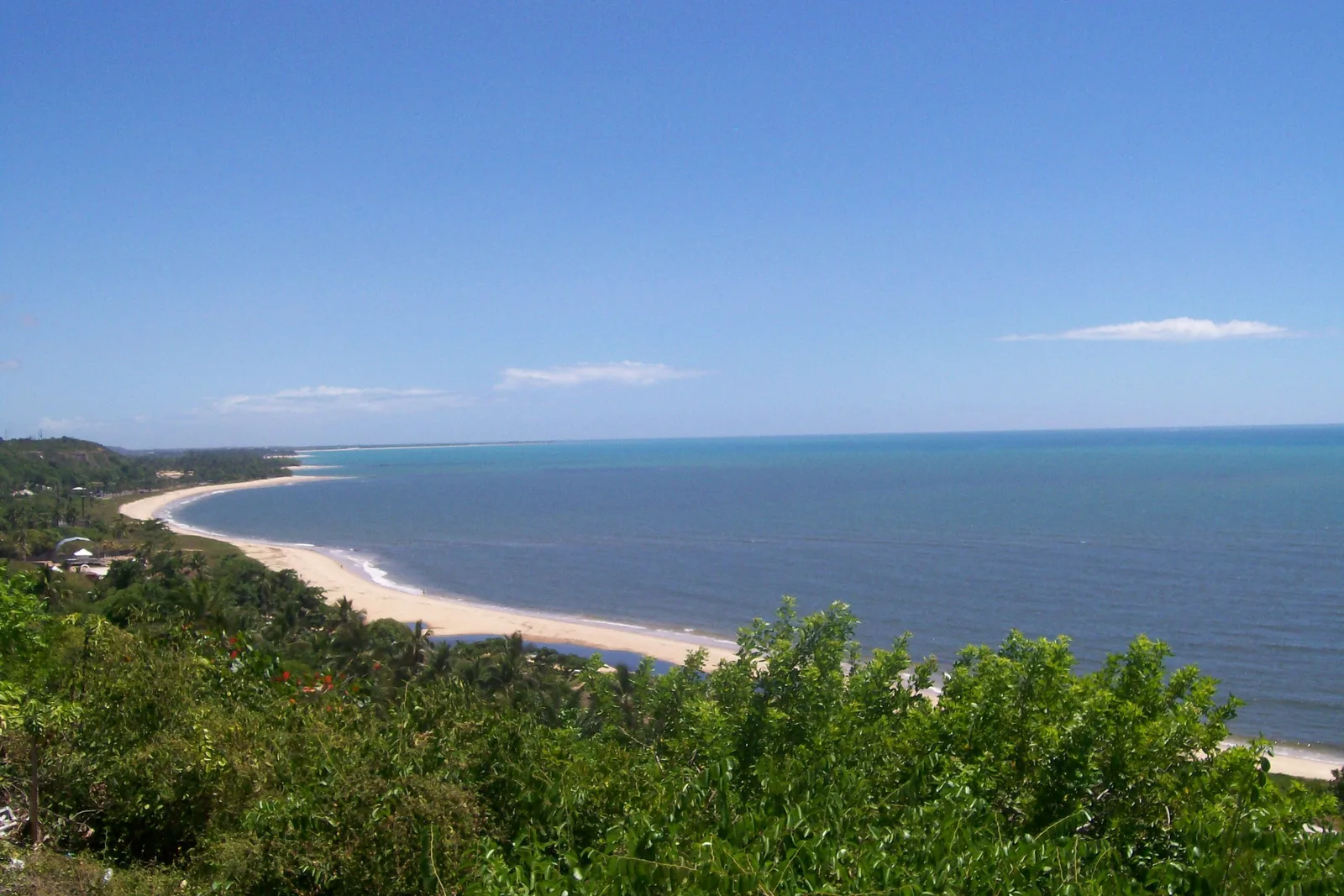 A long curving beach and bay seen from a hill above Trancoso, green scrub in the foreground and the sea deep blue beyond