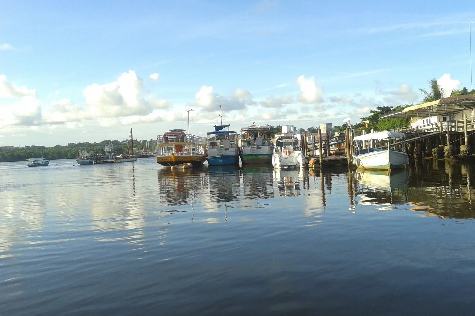 Fishing and tourist boats moored along a pier on the calm Rio Buranhém at Porto Seguro, seen from the deck of the ferry, their hulls reflected in the water
