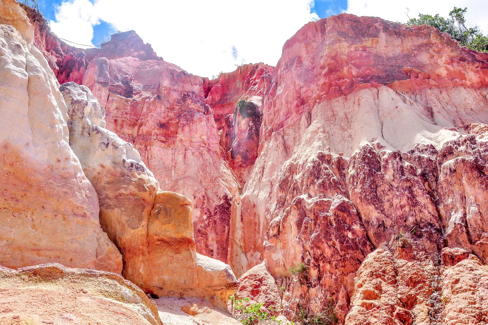 Close view of the eroded cliffs at Arraial d’Ajuda, deep pink and red layers streaked with white and cream under a blue sky