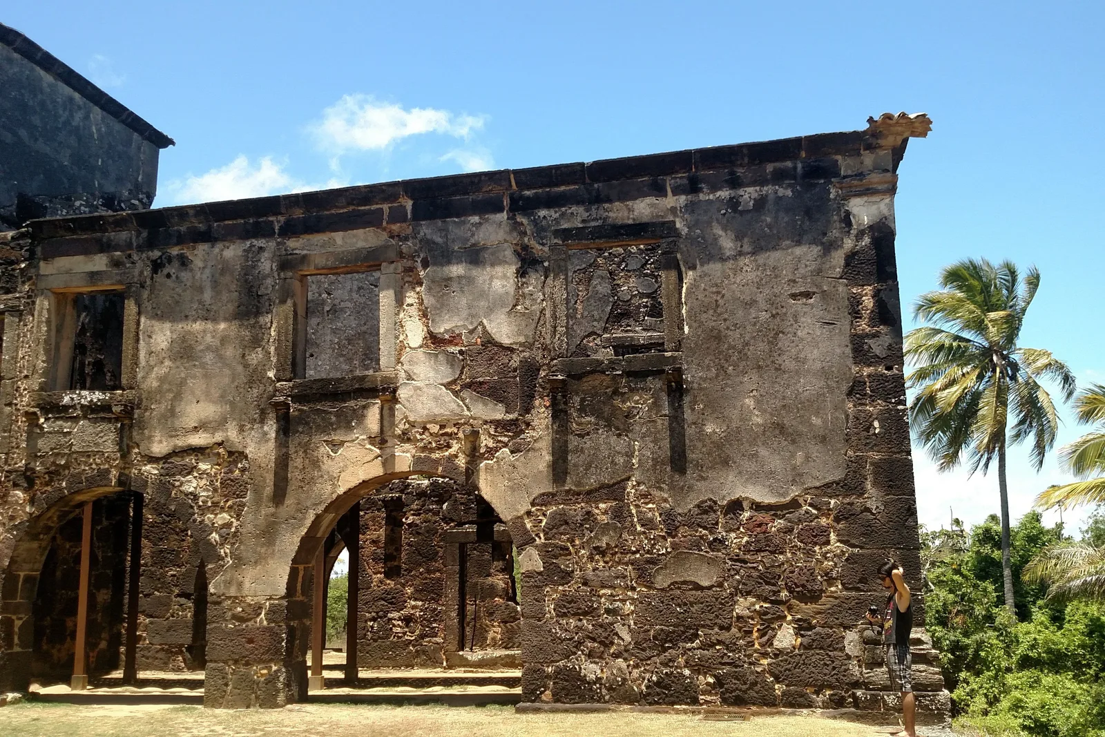 The stone ruins of the Casa da Torre de Garcia d’Ávila, arched doorways open to a blue sky, palms at the edge