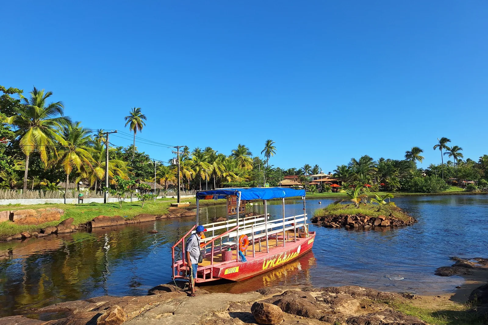 A red and blue river boat tied up on the Imbassaí river, palms along the bank