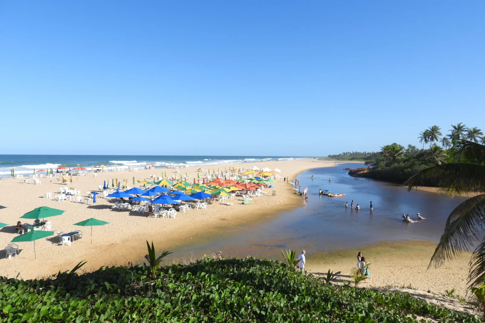 At Imbassaí the river runs along the back of the beach to the sea, bright umbrellas on the sand between them