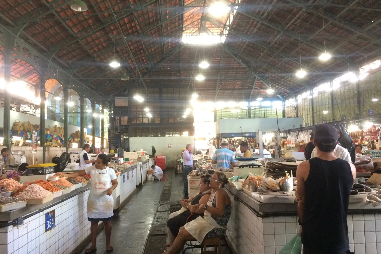 Inside the Mercado de São José in Recife: an aisle of tiled counters stacked with produce under a high iron and glass roof, with traders and shoppers along it