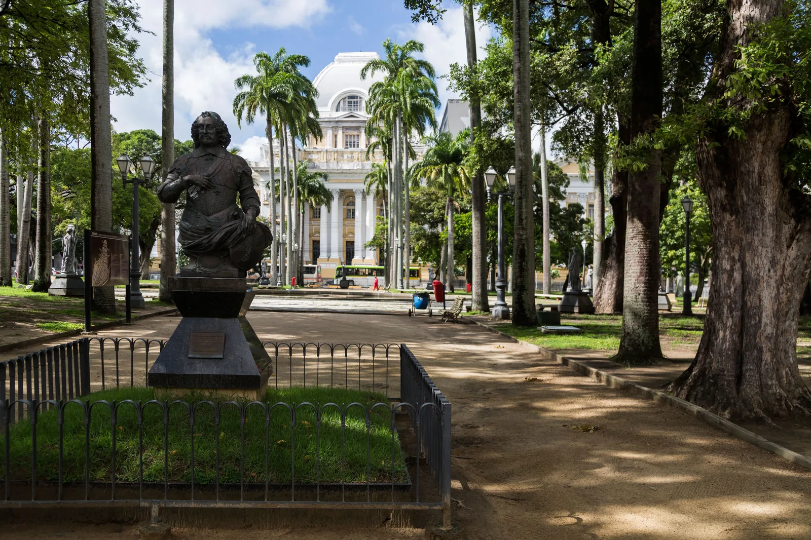 The Praça da República in central Recife: a statue on a plinth under enormous shade trees and royal palms, with a pale nineteenth-century public building behind