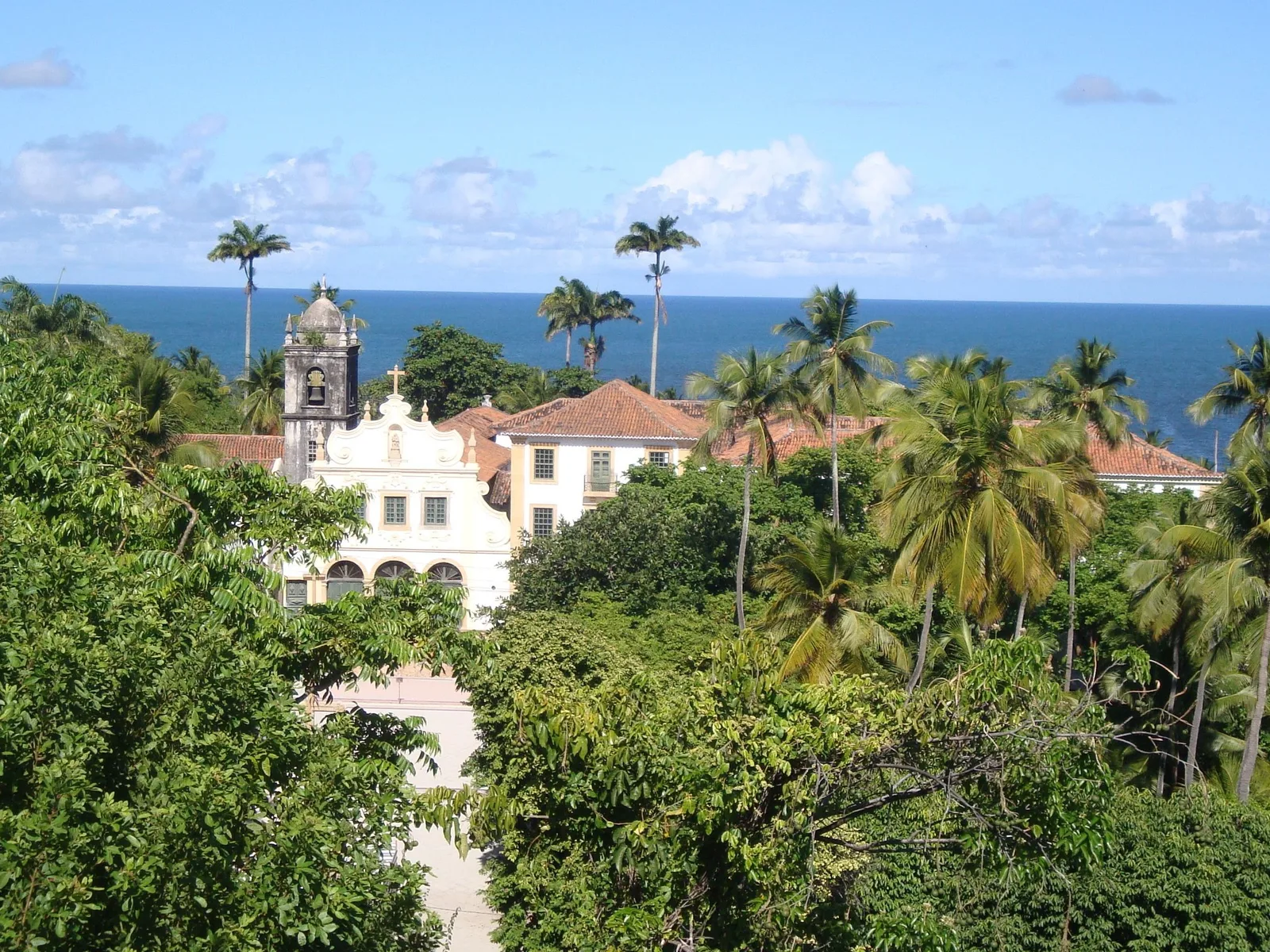 Olinda from above, a white colonial church among palms and terracotta roofs with the Atlantic behind — one of the historic buildings the festival takes over