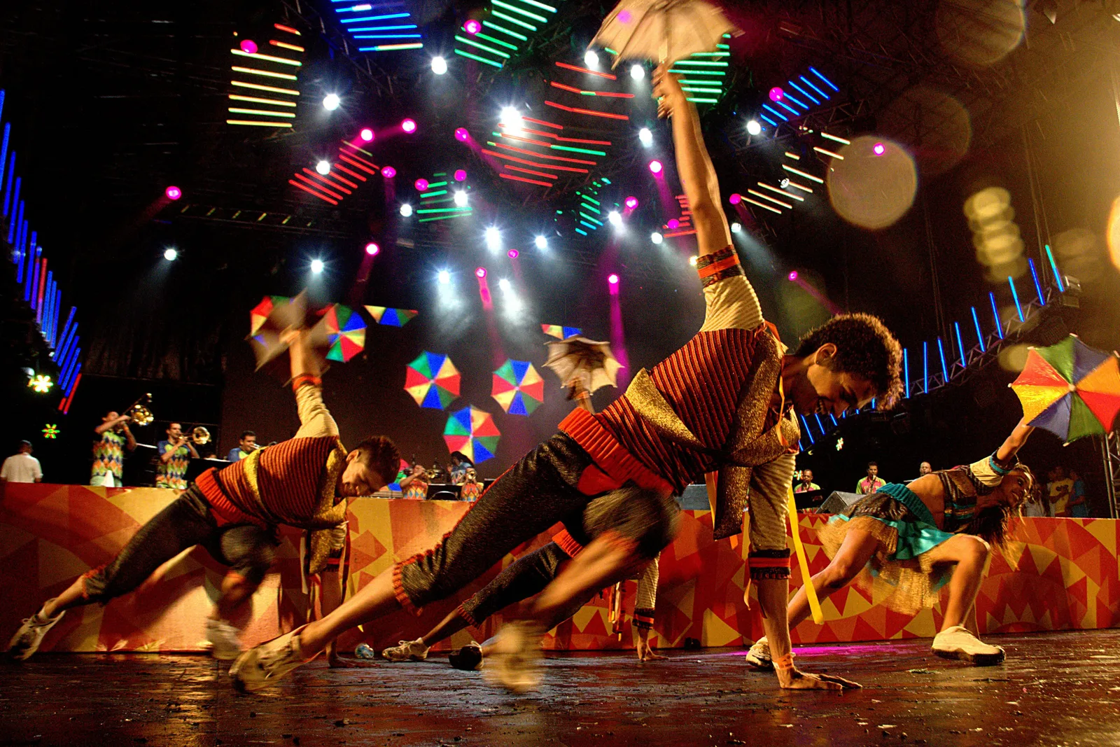 Frevo dancers mid-leap under stage lights, small bright umbrellas held above their heads