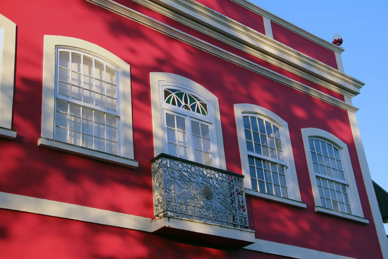The facade of a colonial townhouse in Olinda painted deep red, with white window surrounds and an iron balcony