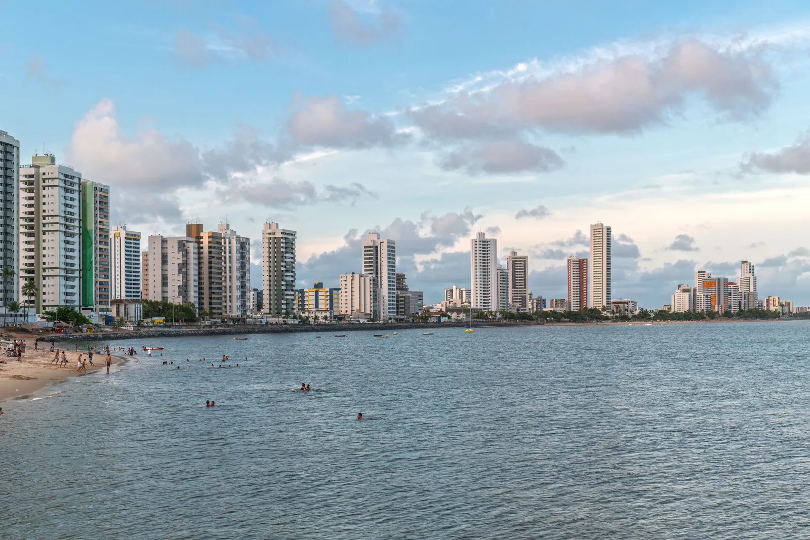 The shoreline north of Recife with people in the water some way out from the sand, and the city’s wall of apartment towers running along the coast beyond