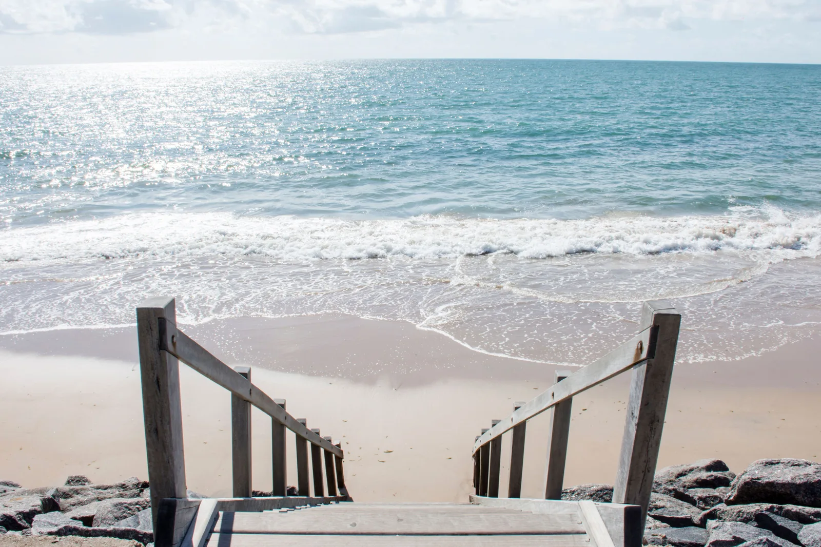A wooden staircase down onto an empty beach north of Recife, dark reef rock along the waterline and the sea running up the sand