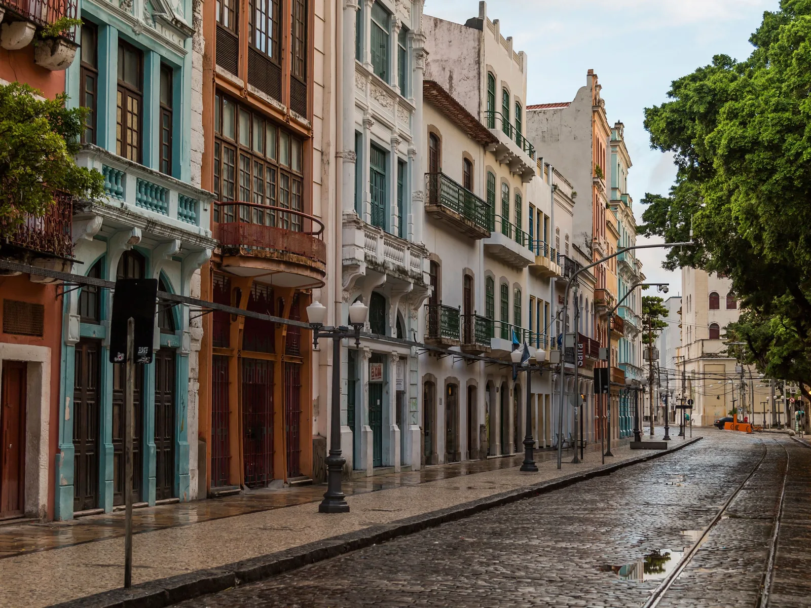 A narrow street of tall colonial townhouses in Recife Antigo after rain, their facades painted green, ochre and blue