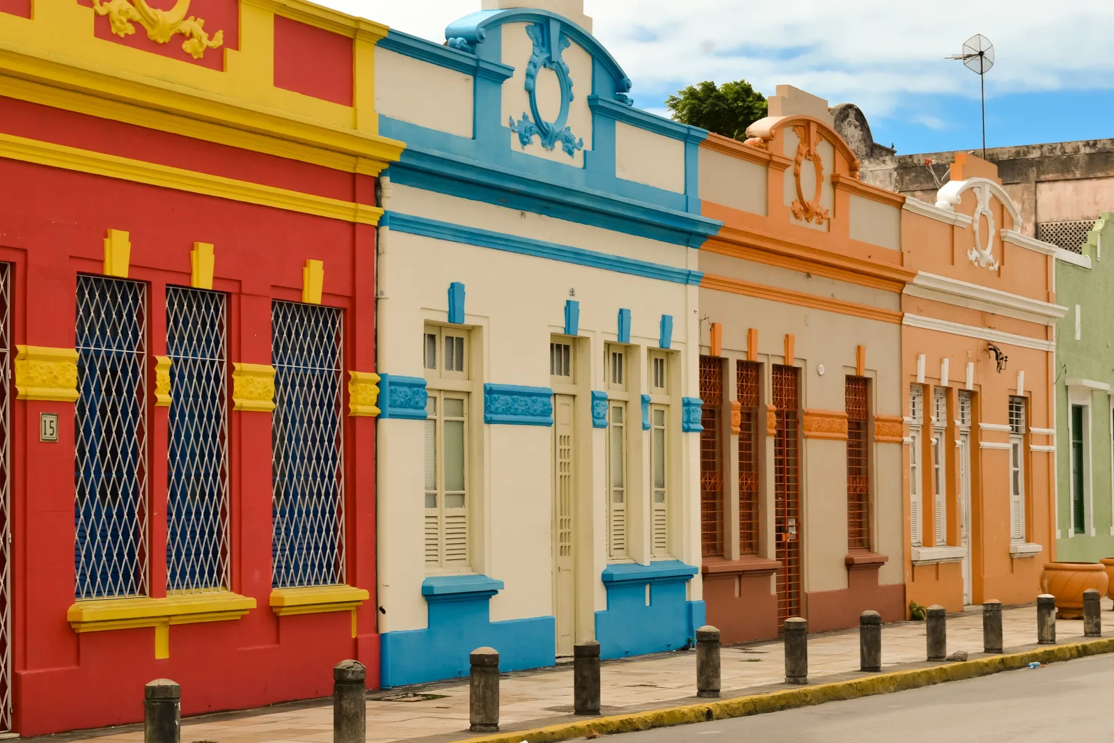 A row of colonial townhouses in Olinda painted red, cream, orange and blue, with barred windows and tall shuttered doors onto the street