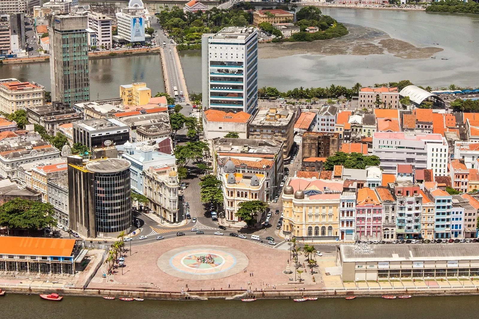 The island of Recife Antigo from the air, the circular plaza of Marco Zero on its quay, colonial rooftops behind it and the harbor and city towers around