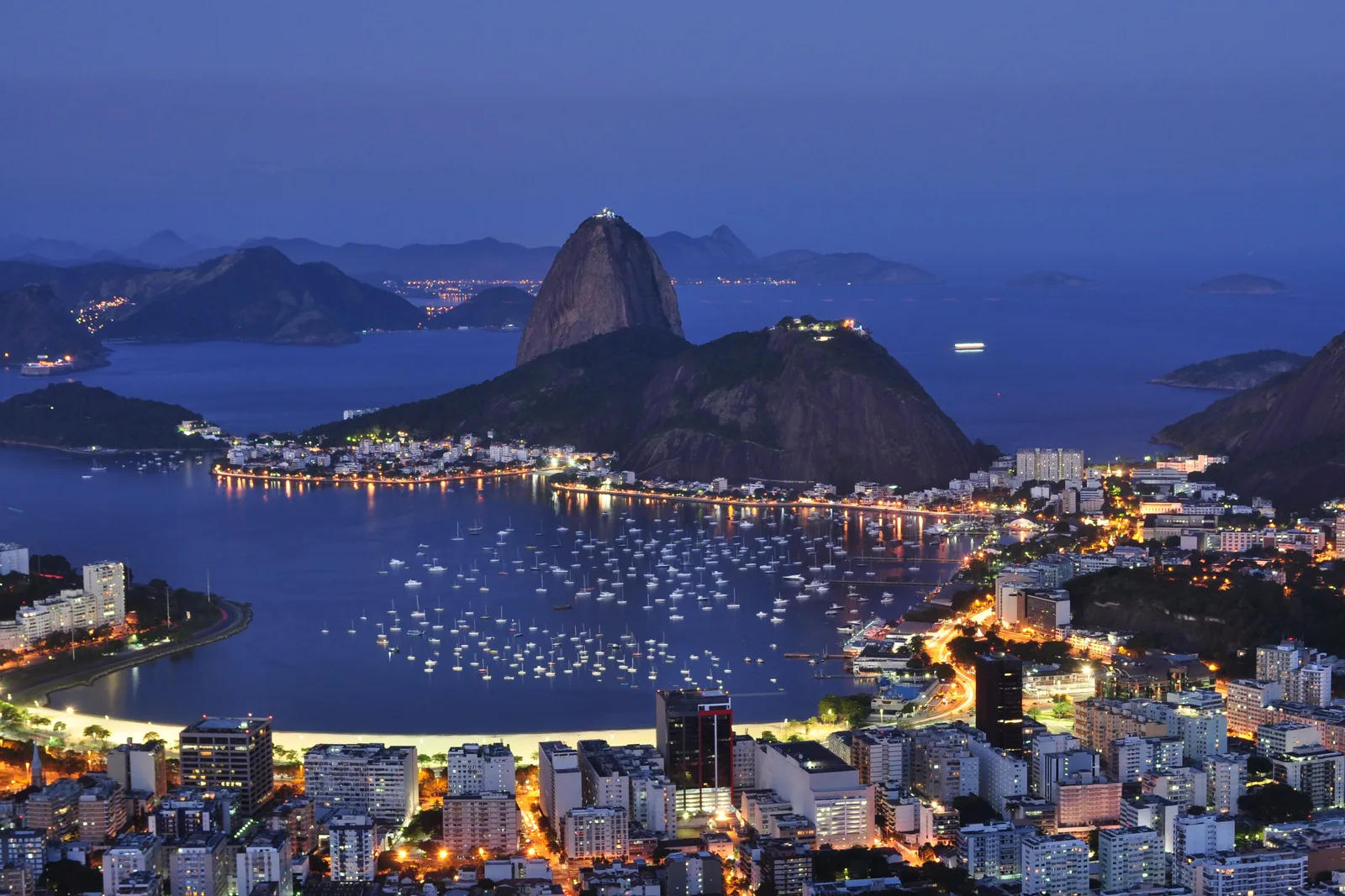 The view from Mirante Dona Marta at dusk: Botafogo bay curving below with its lit marina, and Sugarloaf standing at the mouth of Guanabara Bay