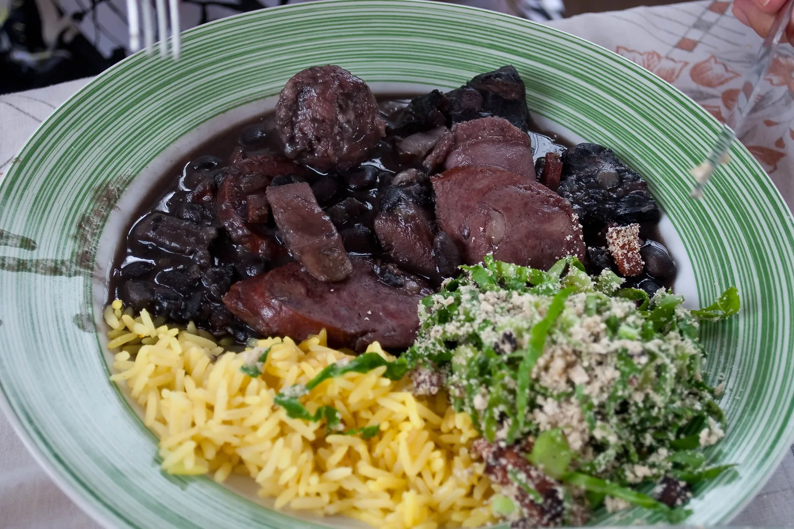 A plate of feijoada: black bean and pork stew alongside rice, farofa and finely shredded collard greens
