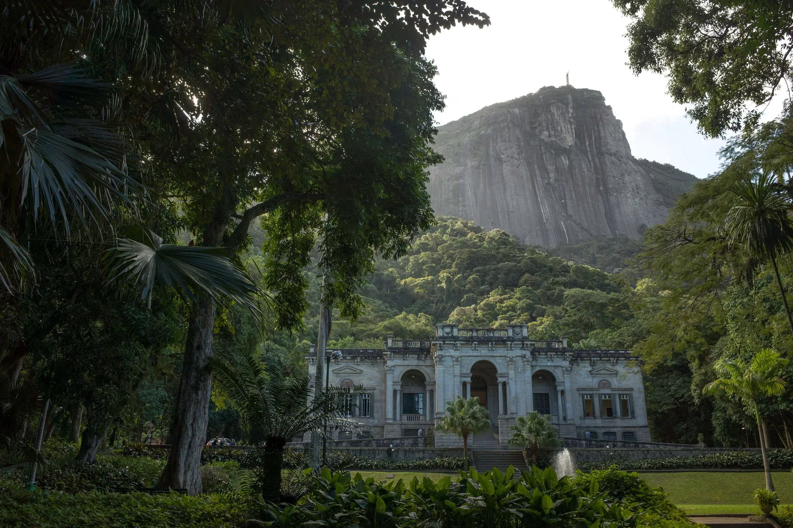 The Parque Lage mansion seen from its gardens, with the bare rock of the mountain rising directly behind it through the trees