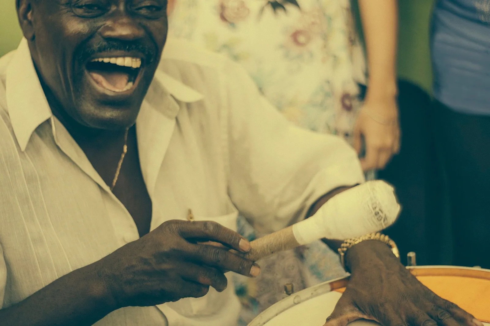 A samba musician playing a hand drum at close range, mid-song and laughing