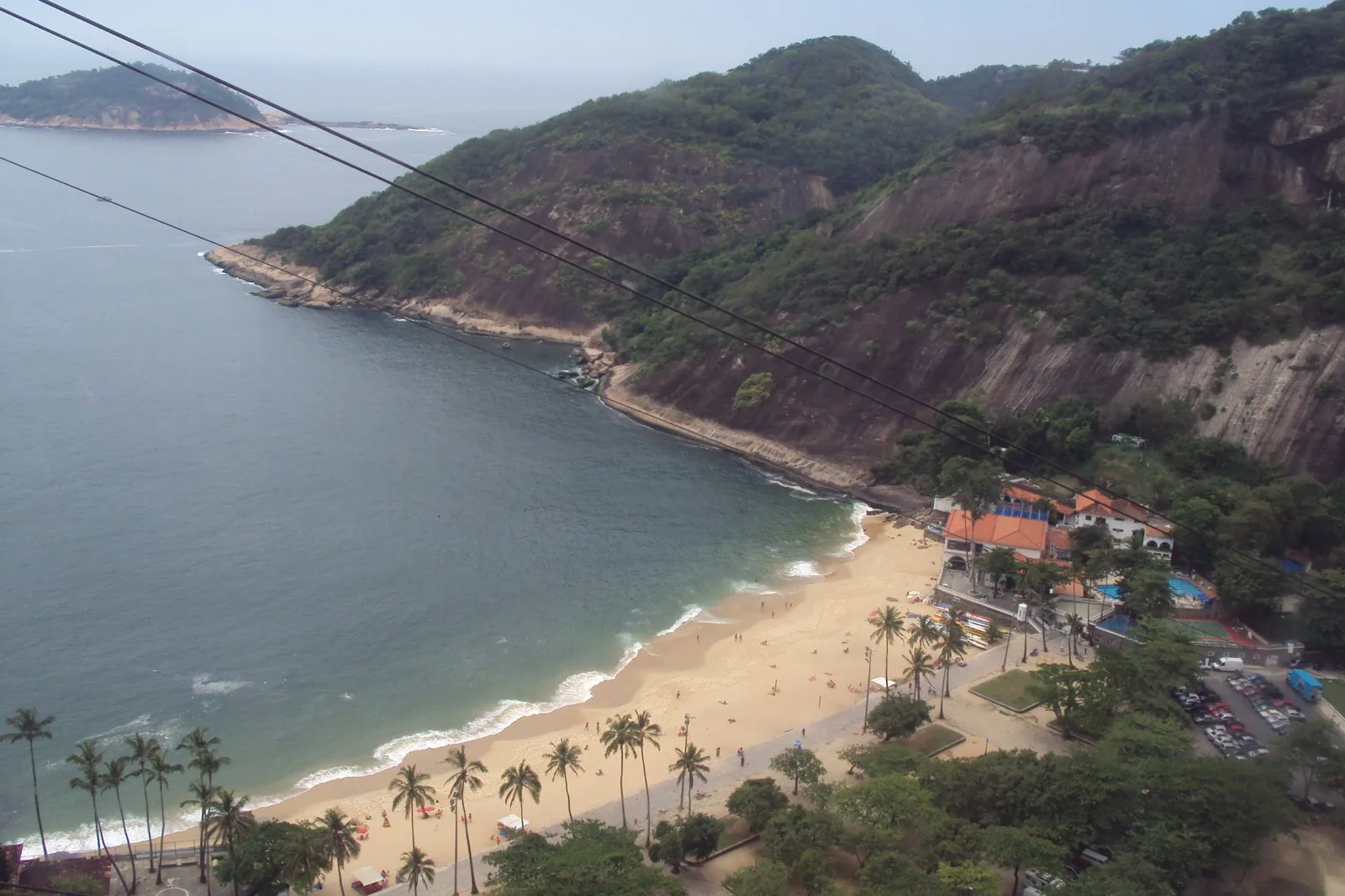 Praia Vermelha seen from above, a short crescent of sand backed by palms and buildings with the forested slope of Morro da Urca behind