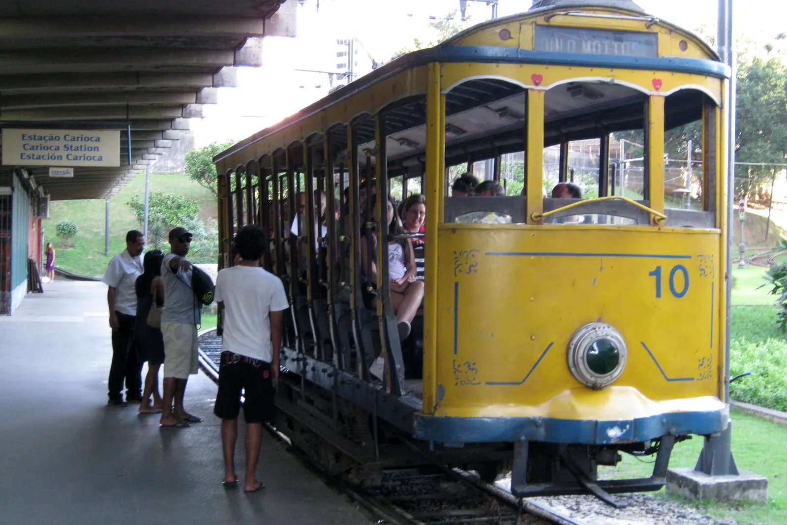 The open-sided yellow Santa Teresa tram waiting at its terminus, passengers standing beside it on the platform