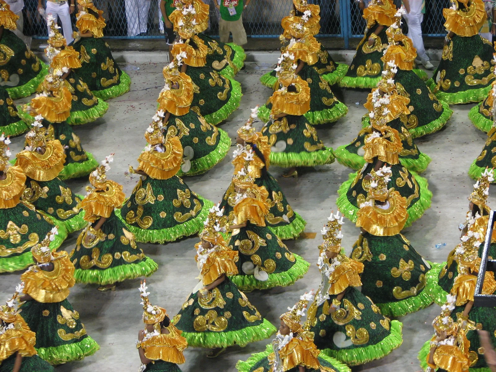 Ranks of samba school dancers in matching green and gold costumes, parading in formation at Carnaval