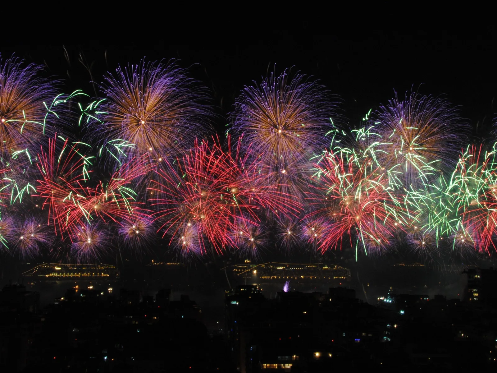 A wall of New Year’s Eve fireworks bursting over the bay, the lit waterfront below