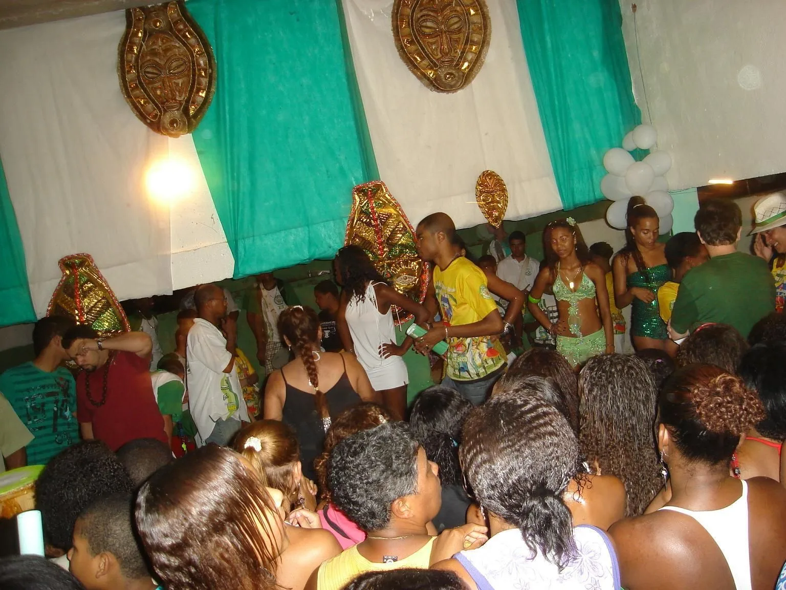 A samba school rehearsal in a packed hall, dancers in costume pressed in among the crowd