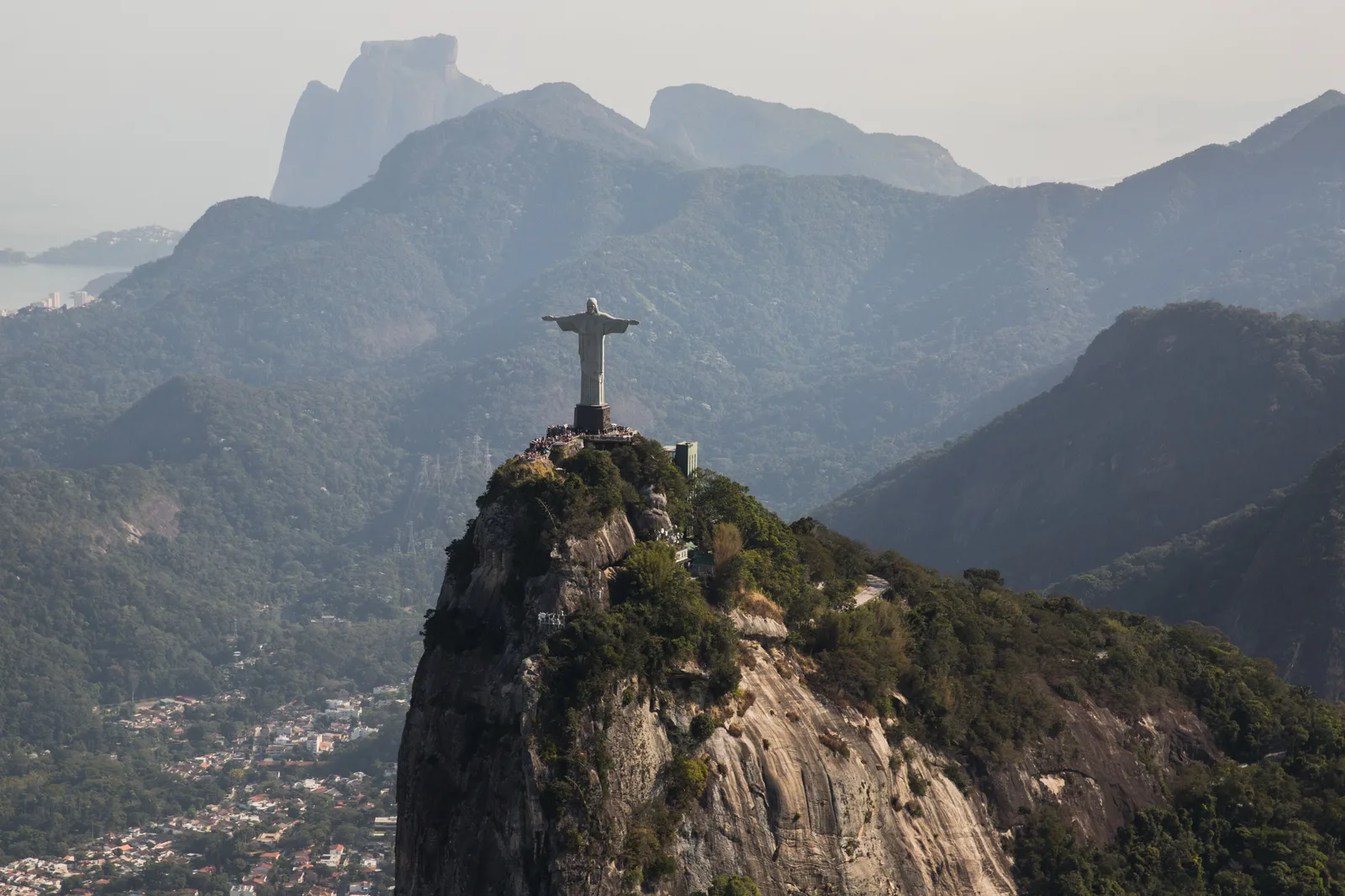 Christ the Redeemer on Corcovado seen from behind, looking out over layers of misty mountains with Pedra da Gávea in the distance