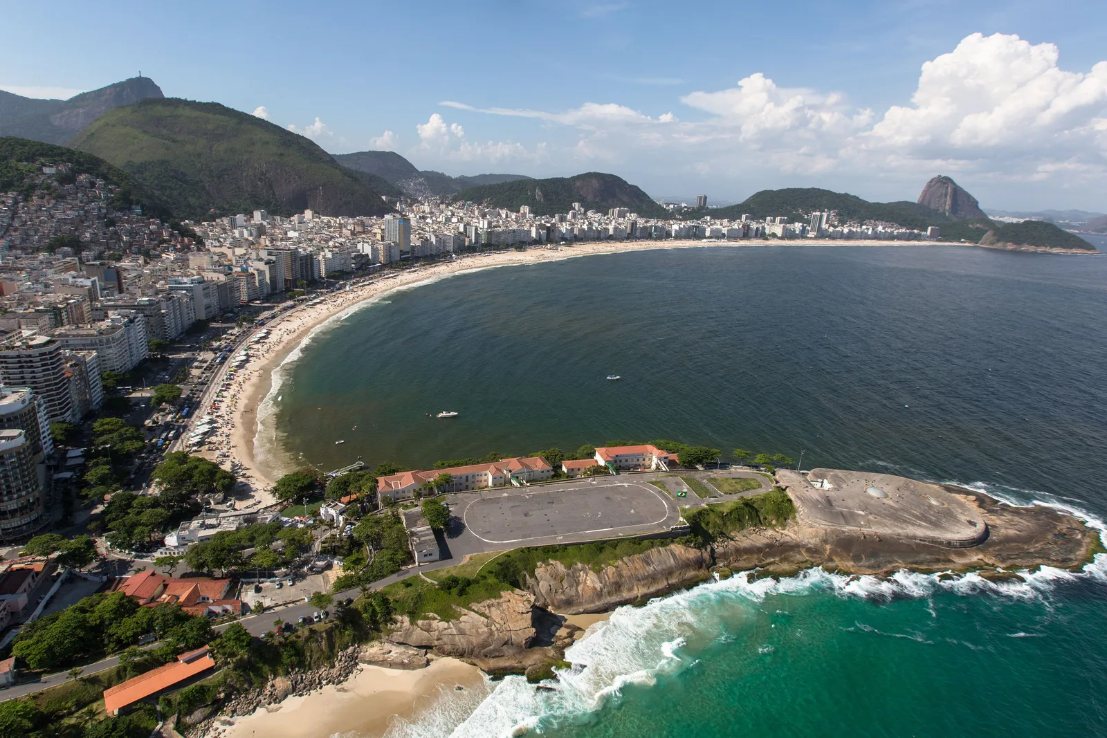 The Copacabana Fort on its rocky point from above, surf breaking below it and the whole curve of Copacabana beach behind