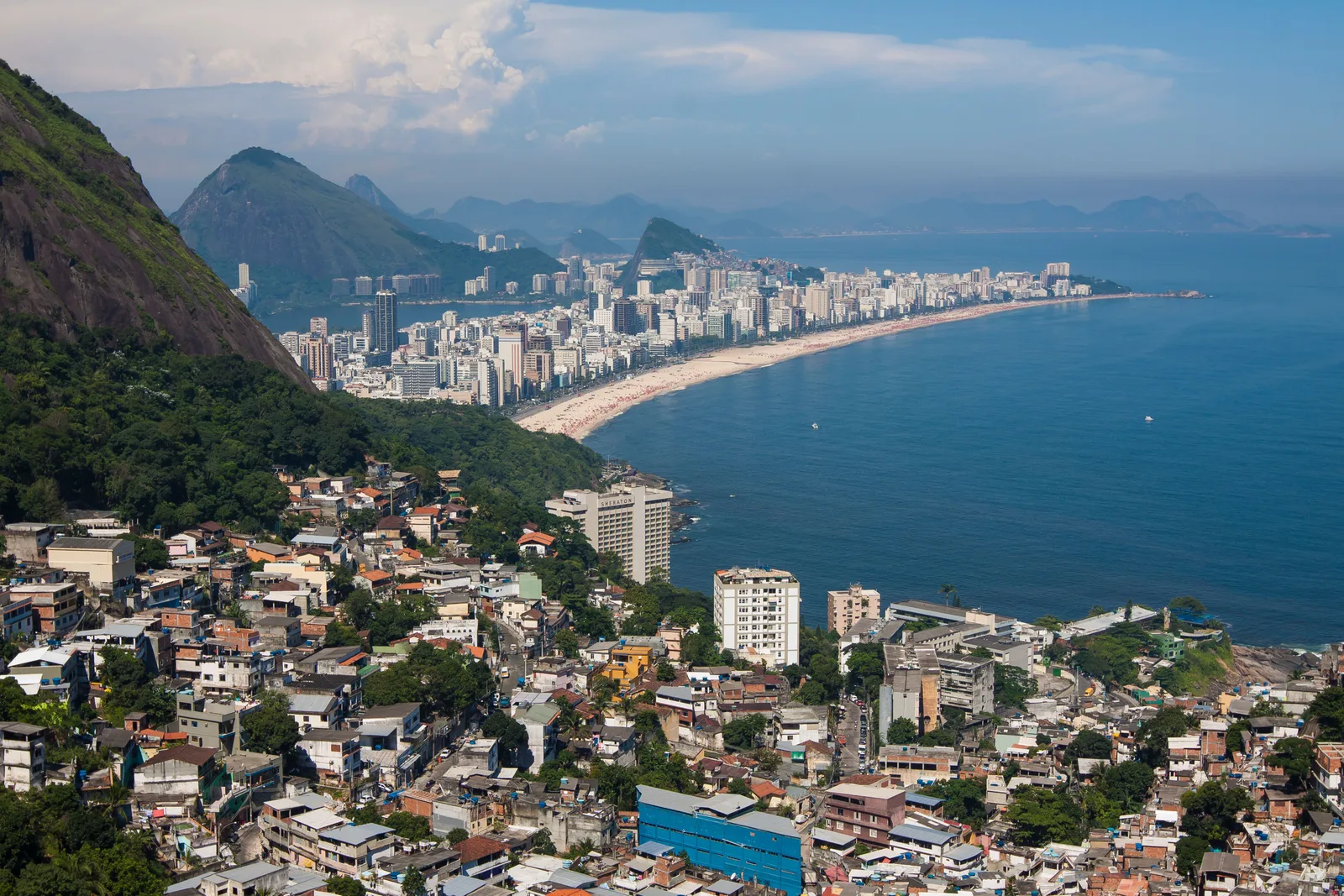 Ipanema and Leblon seen from a hillside, houses stacked down the slope in the foreground and the long beach running toward the mountains
