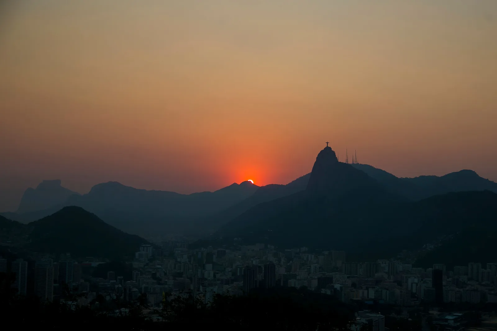 The sun going down in an orange sky behind the dark ridges of Rio’s mountains