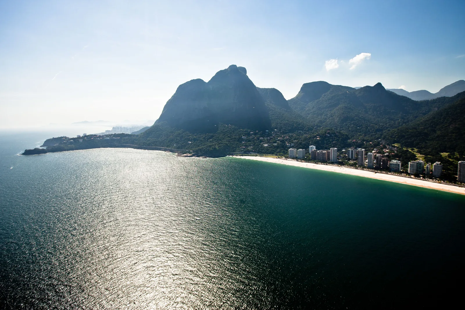 Pedra da Gávea rising above the sea in soft afternoon light, the water glittering in front of it