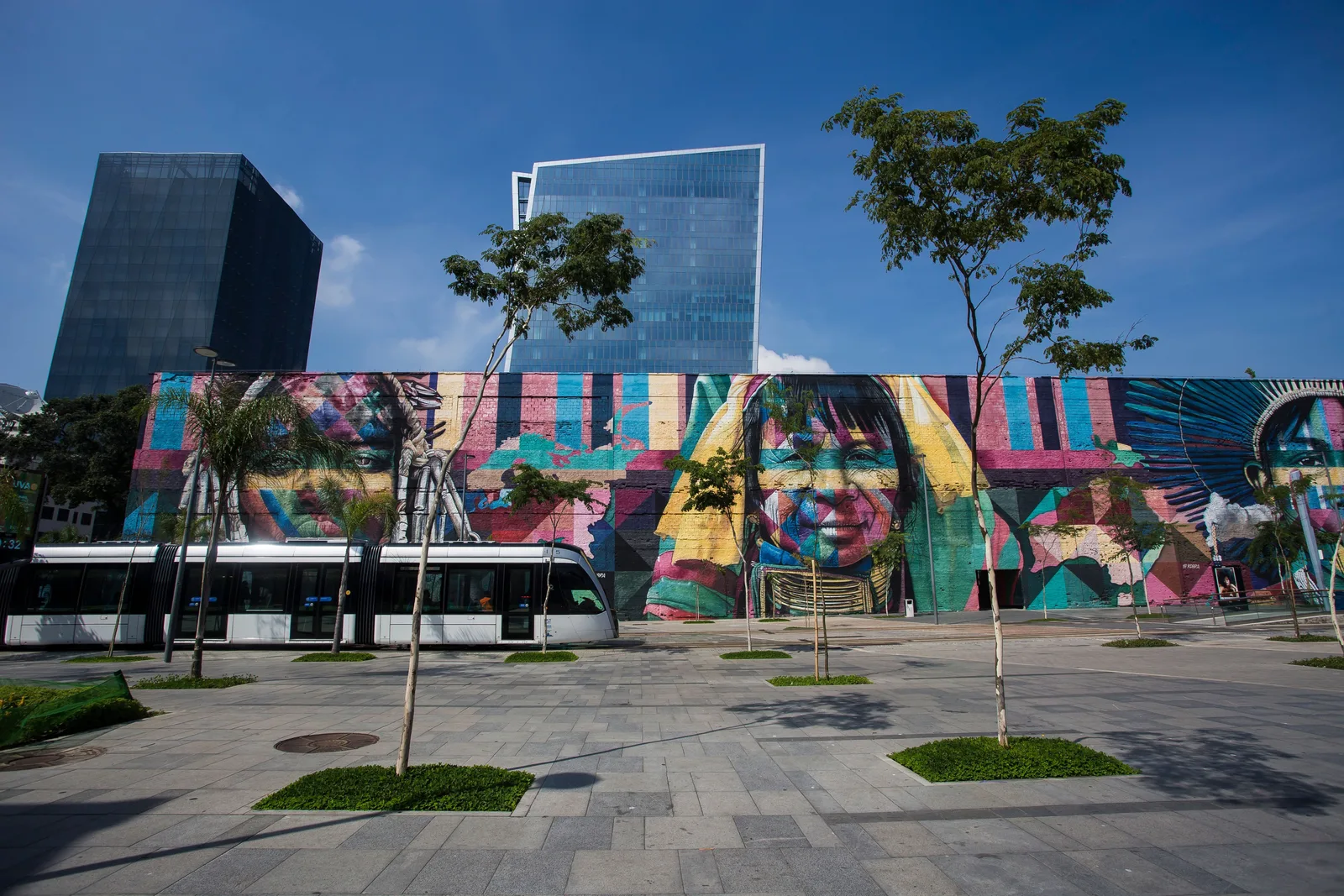 A long, brightly painted mural along the waterfront near Pier Mauá, trees and glass towers above it