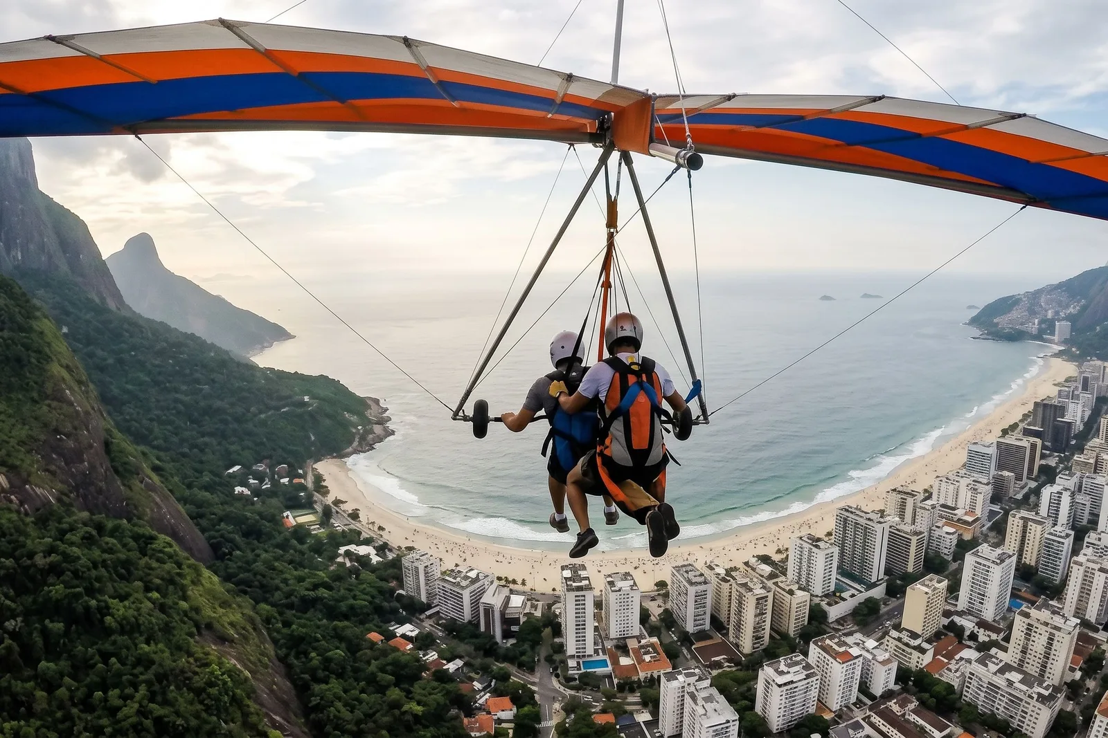 A tandem hang glider banking over São Conrado, the wing filling the top of the frame and the beach and city far below