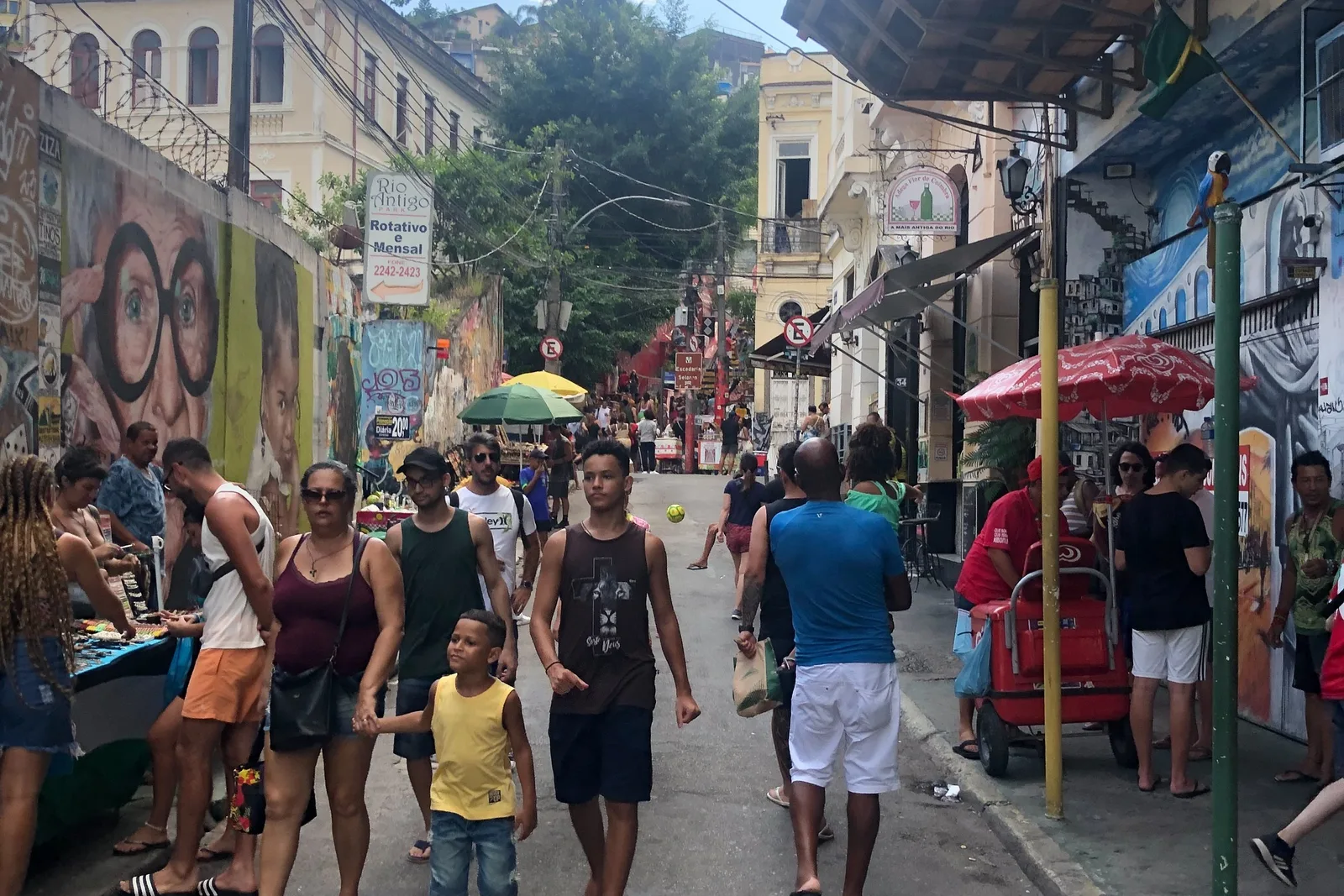 A busy street below Santa Teresa, its walls covered in murals, with stalls and people filling the roadway