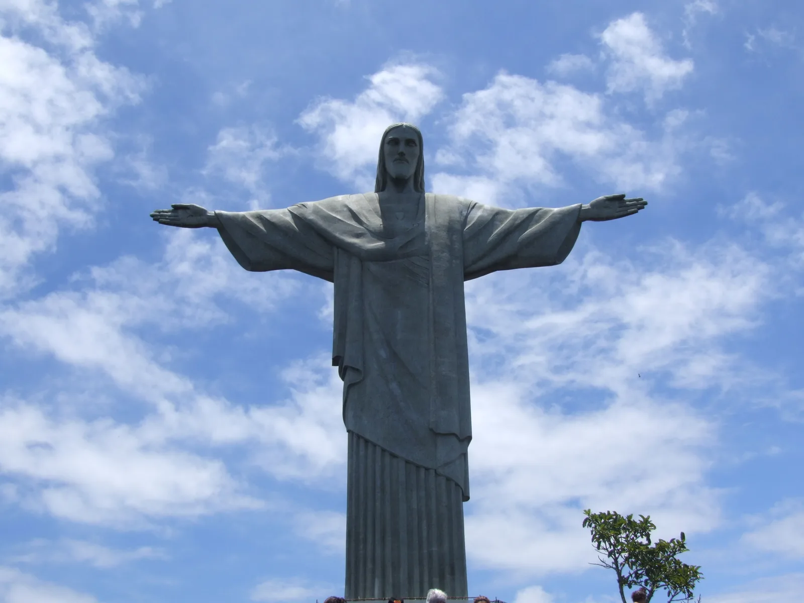 The Christ the Redeemer statue seen from directly below, arms outstretched against a bright sky scattered with cloud